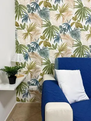 a blue couch in a room with a tropical wallpaper at Quattrociocchi apartment in Bagheria