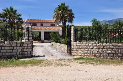 a fence in front of a house with palm trees at Villa Cala Rossa Antonella in Castellammare del Golfo