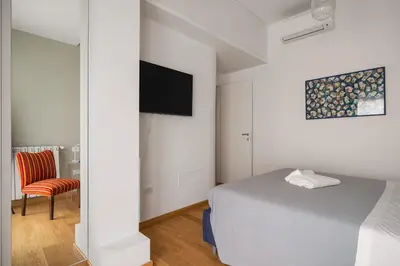 a white bedroom with a bed and a chair at Giusà by DomuSicily in Palermo