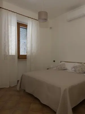 a white bedroom with a bed and a window at La Capinera Holidays in Santa Flavia
