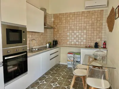 a kitchen with white cabinets and a glass table with chairs at Il Poggio Retreat - Cefalù in Cefalù