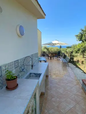 a patio with an outdoor kitchen and an umbrella at Villa L'orizzonte di calabianca in Castellammare del Golfo
