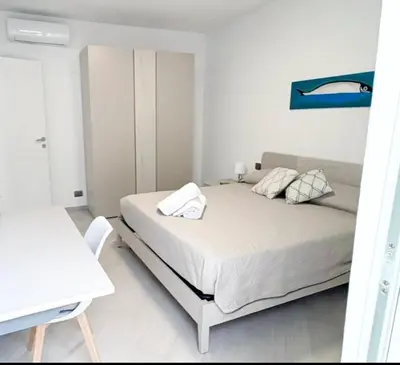 a white bedroom with a bed and a blue painting on the wall at Casa Marinaro in Castellammare del Golfo