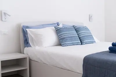 a white bed with blue and white pillows on it at Casa vacanze Marinaro in Castellammare del Golfo