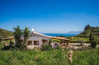 a house in a field with the ocean in the background at Villa Elena 2 Km from the Natural Reserve of Zingaro in Scopello