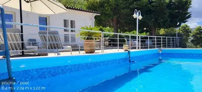 a blue swimming pool with chairs and an umbrella at Villa Ballerina Bianca in Scopello