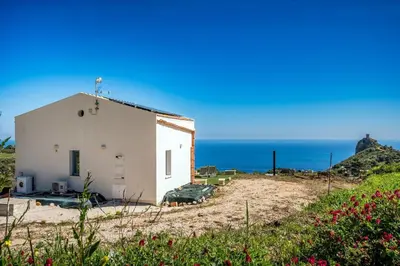 a white building on the beach with the ocean in the background at Villa Holidays Vista Torre Bennistra in Scopello in Scopello