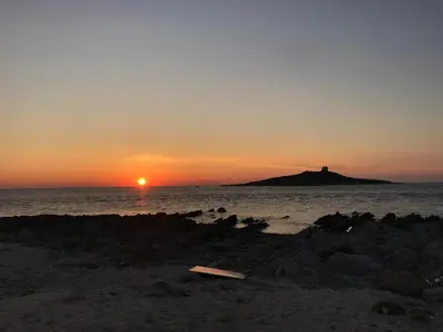 a sunset on the beach with a lighthouse in the distance at La casetta di Toto' in Isola delle Femmine