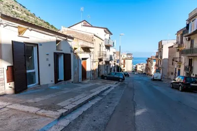 an empty city street with cars parked on the street at White Home in Castellammare del Golfo