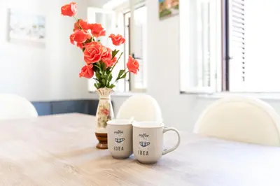 two coffee cups on a table with a vase of flowers at Gennaro Holidays Appartament in Corleone