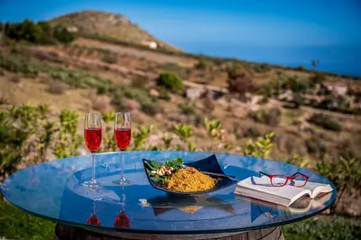 a glass table with a plate of food and two wine glasses at Villa Pharus Scopello in Scopello