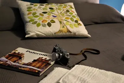 a book and a camera on a couch with a pillow at La Via delle Biciclette in Palermo
