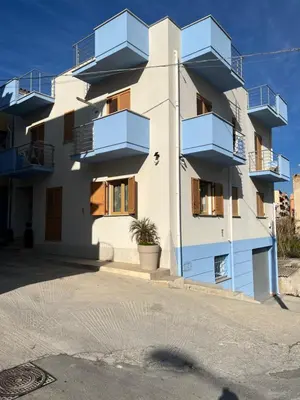 a white building with blue balconies on a street at Mare Blu Apartament in Balestrate