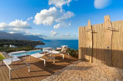 a patio with a pool and chairs and the ocean at Villa Corallo Cala Bianca in Castellammare del Golfo