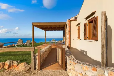 a house with a wooden walkway next to the ocean at Villa Corallo Cala Bianca in Castellammare del Golfo
