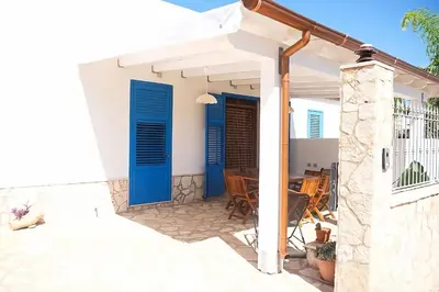 a white house with blue doors and a table at Villa Indipendente Tranquillità e Relax in San Vito lo Capo