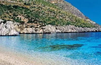 a beach with blue water next to a mountain at Ancilinas House in Castellammare del Golfo