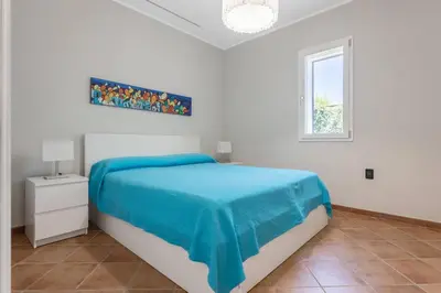 a white bedroom with a blue bed and a window at Villa NìMia in Castellammare del Golfo
