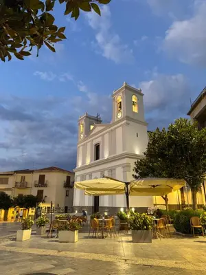 a white building with a clock tower with tables and umbrellas at Le Casette di campagna #2 in Campofelice di Roccella