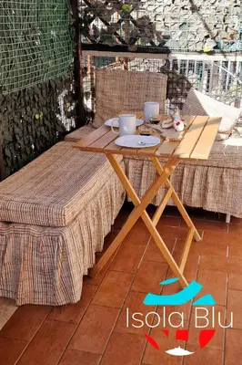 a wooden table with two chairs and a table with cups and plates at Isola Blu Casa a pochi passi dal mare in Isola delle Femmine
