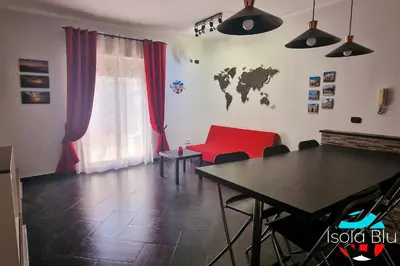 a living room with a table and a red couch at Isola Blu Casa a pochi passi dal mare in Isola delle Femmine