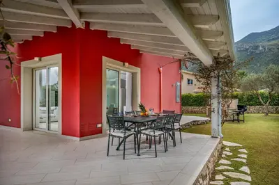 a table and chairs on a patio with a red wall at Villa Jacqueline con piscina privata 8 posti letto in Scopello
