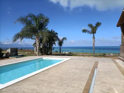 a swimming pool with palm trees and the ocean at Villa Panorama in Trappeto