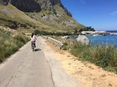 a woman riding a bike down a dirt road at Ashur 163 - Mondello in Palermo