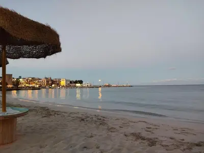 a beach with a straw umbrella and the ocean at Mondello Villetta Giusi in Mondello