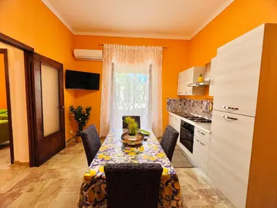 a kitchen with a table with chairs and a kitchen with orange walls at Orange House in Isola delle Femmine