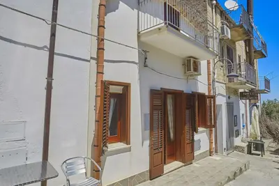 a building with wooden doors and a bench on a street at Casa Maria Stella Scopello in Scopello