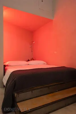 a bedroom with a red wall with a bed in it at Lofterì by DomuSicily in Palermo