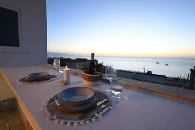 a table with plates and wine glasses and a view of the ocean at Riad Casa Vacanze in Terrasini