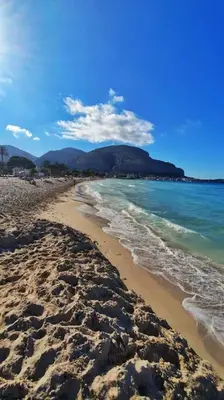 a sandy beach with the ocean and mountains in the background at apartment by the sea Mondello beach in Palermo