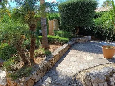 a garden with palm trees and a stone wall at Castellaccio Scopello Villetta con piscina in Scopello