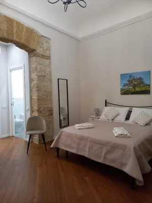 a white bedroom with a large bed and a chair at Residenza del Massimo in Palermo