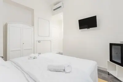 a white bedroom with a bed and a flat screen tv at Aragona House in Palermo