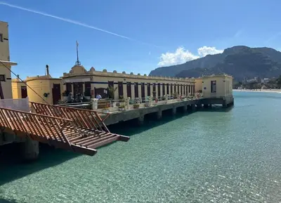 a pier on the water with buildings and mountains at La Casa Di Mitì in Palermo