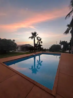 a swimming pool with palm trees and a sunset at Sunset Holiday House in Cefalù