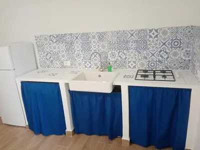 a kitchen with a sink and a stove with blue curtains at Mediterranea casa vacanza in Capaci