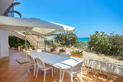 a table and chairs with an umbrella and the ocean at Villa Azzurra a pochi passi dal mare in Castellammare del Golfo
