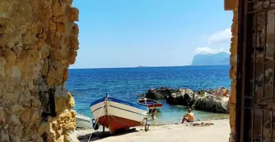 a boat on a beach with people in the water at House of Lady in Carini
