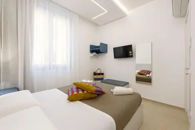 a white bedroom with two beds and a tv at Residence Mazzini in San Vito lo Capo