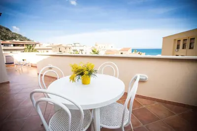 a white table with chairs and a vase of flowers on a balcony at Appartamento Le Terrazze in Castellammare del Golfo