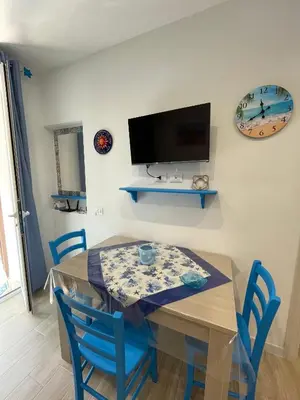a dining room table with blue chairs and a tv at La Casetta di Isola in Isola delle Femmine