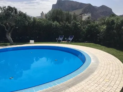 a blue swimming pool with two chairs in a yard at Villa dell'Ulivo - by DomuSicily in Terrasini