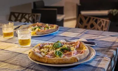 two pizzas on plates on a table with beer at Senza Pensieri Holiday Home in Balestrate