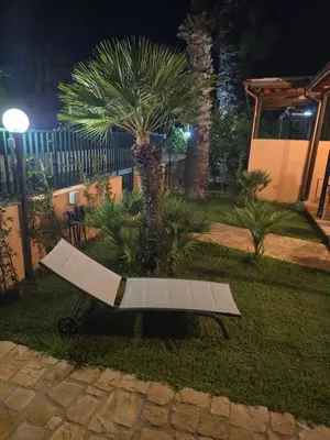 a bench sitting in the grass next to a palm tree at Villetta Viola in San Vito lo Capo
