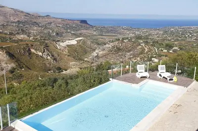 a swimming pool with two chairs and a view of the ocean at Villa del Poggio in Scopello