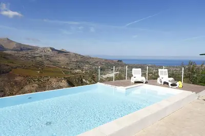 a swimming pool with two chairs and the ocean at Villa del Poggio in Scopello